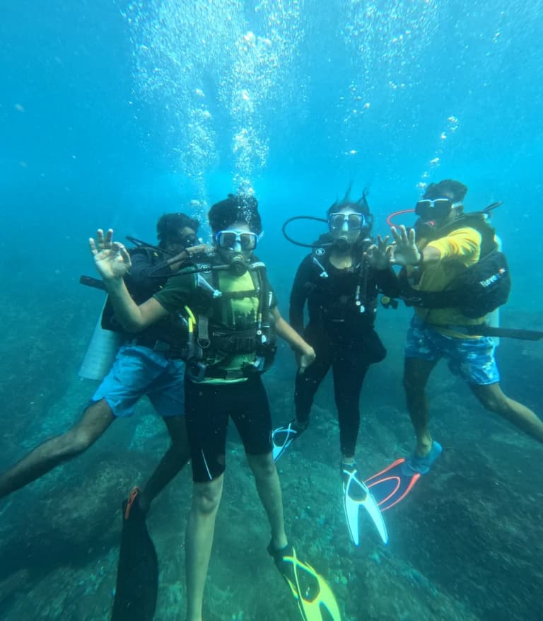 Three divers underwater posing with OK and victory signs