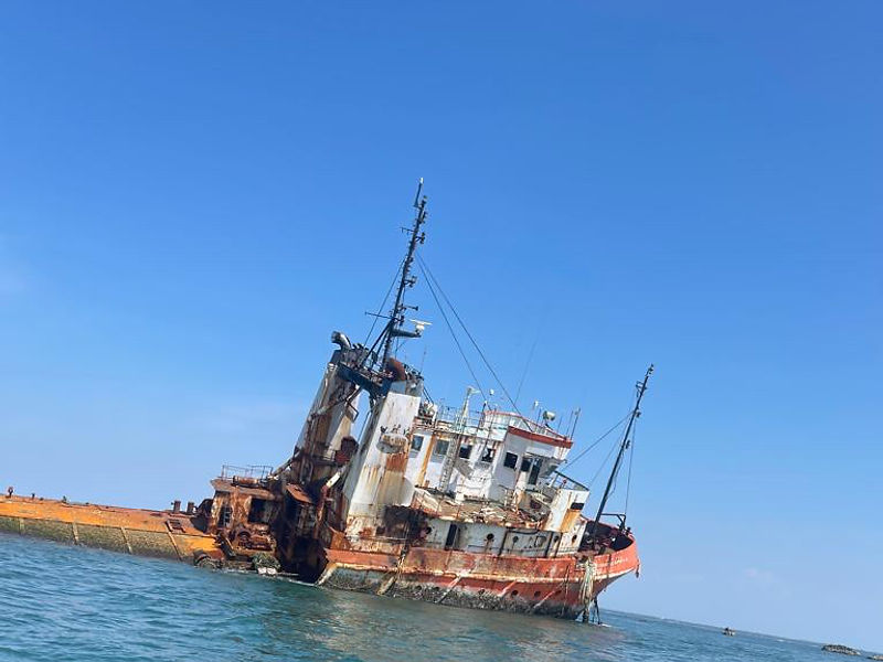 Large rusted shipwreck listing to one side in the ocean