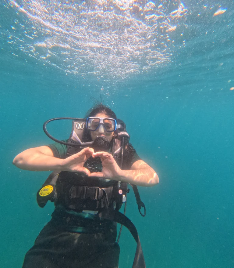 Female diver in green t-shirt making a heart shape with hands underwater
