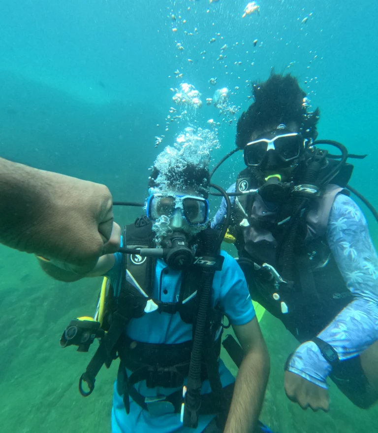 Male diver in blue shirt taking an underwater selfie with a fist bump