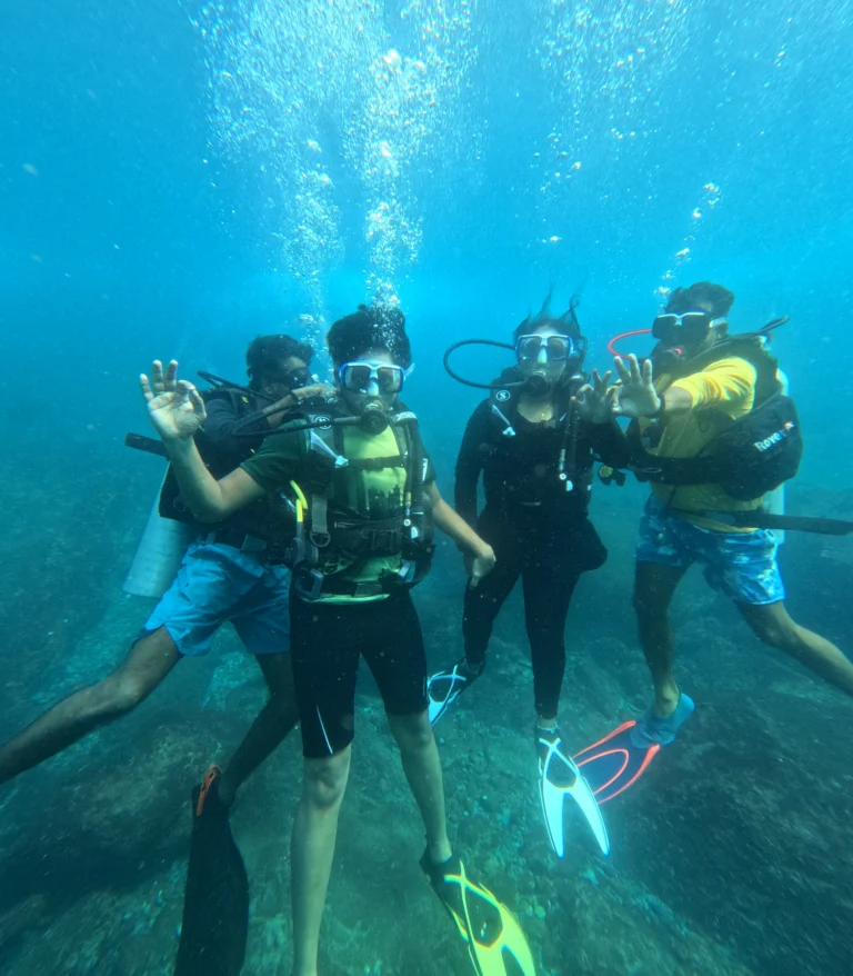 Three divers underwater posing with OK and victory signs
